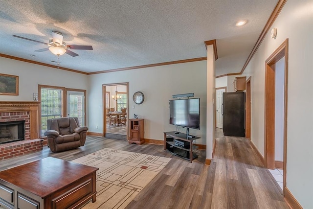 living room featuring crown molding, a brick fireplace, hardwood / wood-style flooring, ceiling fan, and a textured ceiling