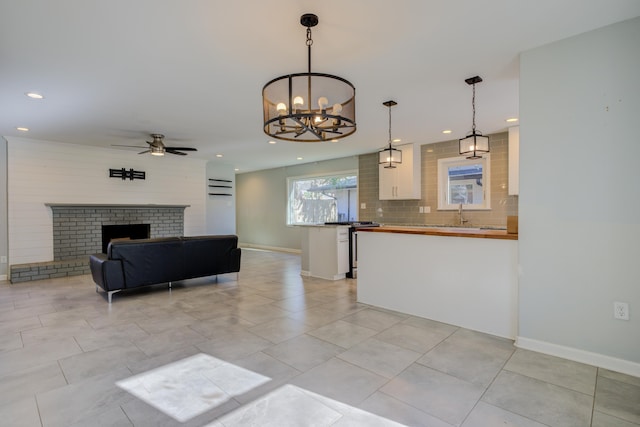 living room featuring a fireplace, light tile patterned floors, ceiling fan with notable chandelier, and sink