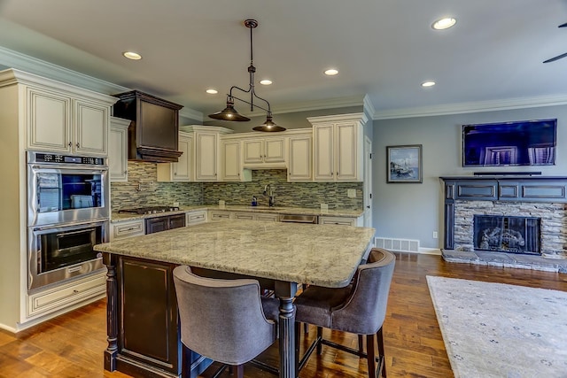 kitchen featuring cream cabinetry, appliances with stainless steel finishes, dark hardwood / wood-style floors, hanging light fixtures, and light stone countertops