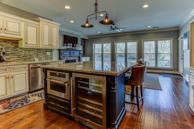 kitchen featuring cream cabinets, appliances with stainless steel finishes, beverage cooler, light stone counters, and a breakfast bar