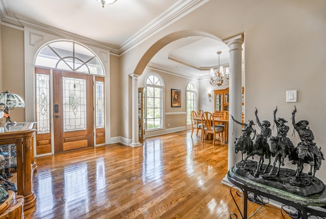 foyer featuring light hardwood / wood-style flooring, crown molding, a notable chandelier, and ornate columns