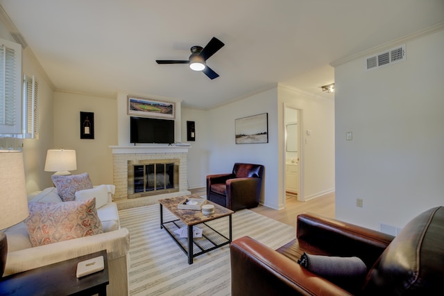 living room with a fireplace, light hardwood / wood-style floors, ceiling fan, and crown molding