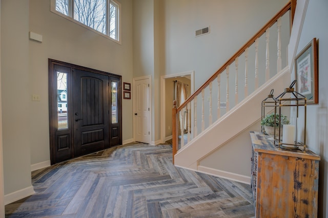 entryway featuring dark parquet flooring and a towering ceiling