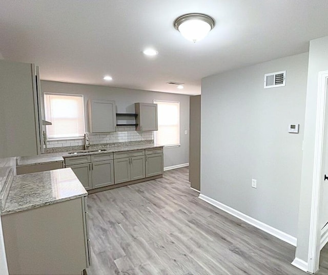 kitchen featuring gray cabinetry, sink, light stone counters, backsplash, and light hardwood / wood-style floors