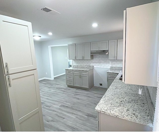 kitchen with gray cabinets, light stone countertops, light hardwood / wood-style flooring, and tasteful backsplash