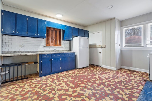 kitchen with white fridge, sink, blue cabinetry, and tasteful backsplash