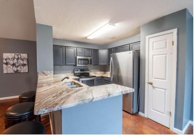 kitchen featuring a kitchen breakfast bar, sink, appliances with stainless steel finishes, light stone counters, and kitchen peninsula