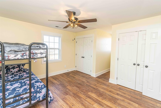 bedroom with ceiling fan, dark hardwood / wood-style flooring, and multiple closets