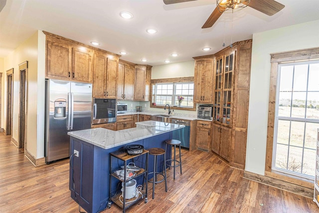 kitchen with a breakfast bar, a center island, sink, light stone countertops, and stainless steel appliances