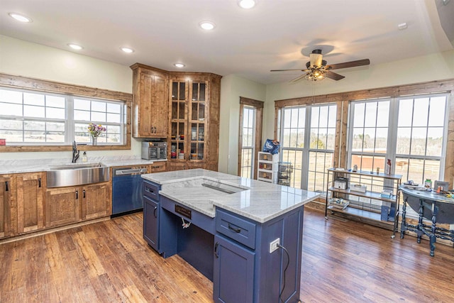 kitchen featuring light stone counters, stainless steel dishwasher, a healthy amount of sunlight, sink, and a center island