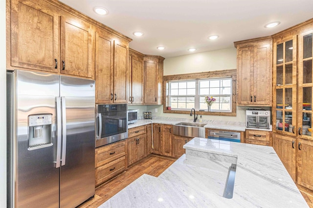 kitchen with light stone countertops, sink, wood-type flooring, and appliances with stainless steel finishes