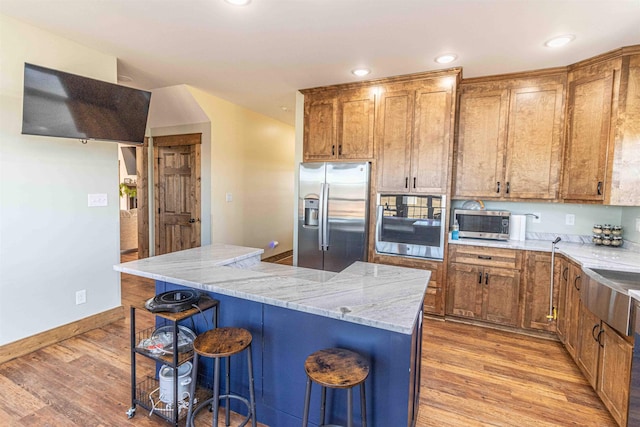 kitchen featuring stainless steel appliances, a kitchen breakfast bar, light stone counters, a kitchen island, and light wood-type flooring