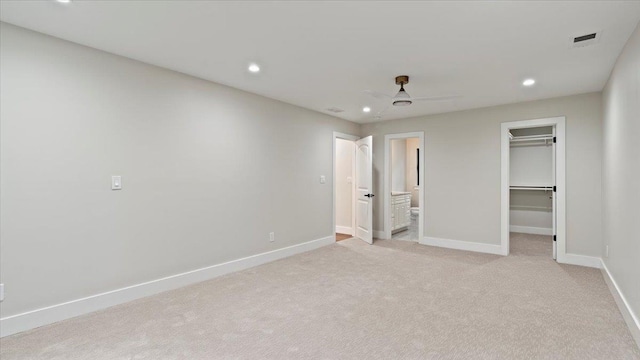 unfurnished bedroom featuring ensuite bathroom, light colored carpet, ceiling fan, a spacious closet, and a closet