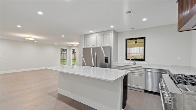 kitchen with light stone countertops, appliances with stainless steel finishes, a kitchen island, sink, and white cabinetry