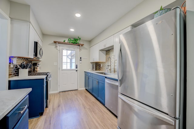 kitchen with white cabinets, sink, blue cabinetry, tasteful backsplash, and stainless steel appliances