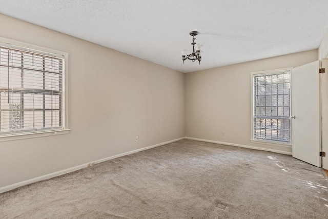 spare room featuring carpet flooring, a textured ceiling, and an inviting chandelier