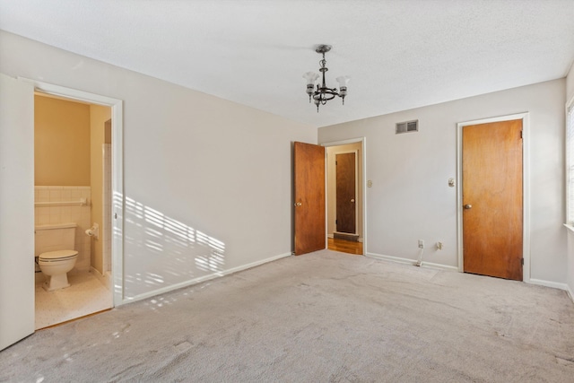 unfurnished bedroom with ensuite bathroom, light carpet, tile walls, and an inviting chandelier