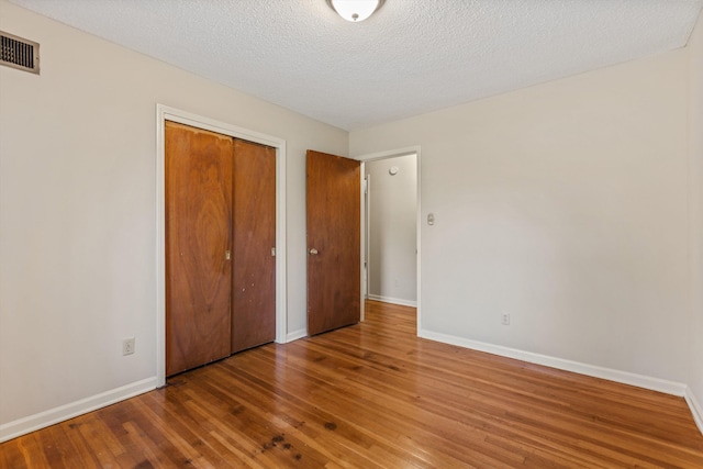 unfurnished bedroom with a closet, a textured ceiling, and hardwood / wood-style flooring