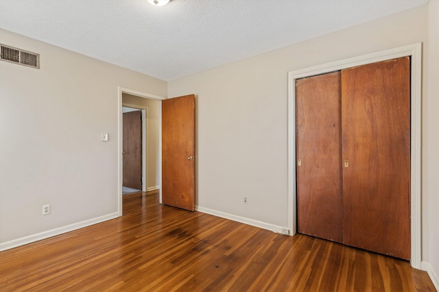 unfurnished bedroom with a textured ceiling, dark hardwood / wood-style floors, and a closet