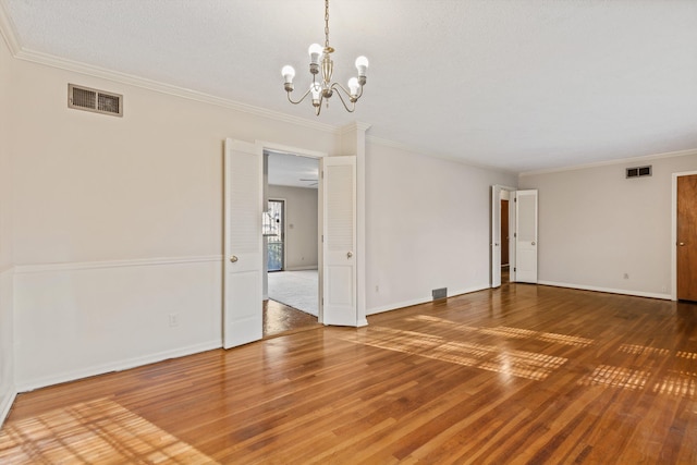 spare room featuring wood-type flooring, crown molding, and a chandelier