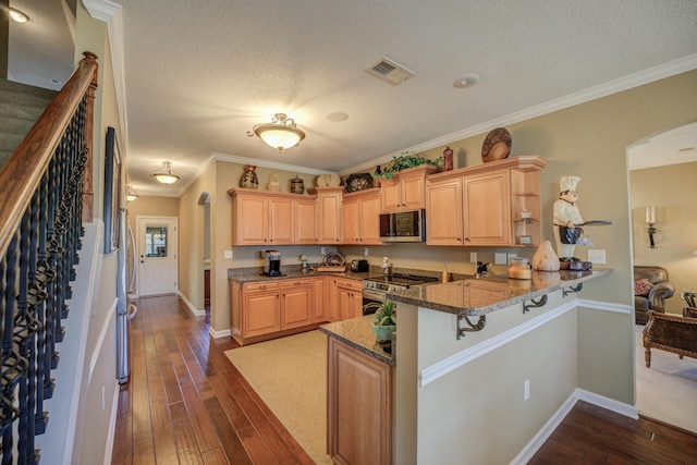 kitchen featuring kitchen peninsula, dark stone counters, stainless steel appliances, and crown molding