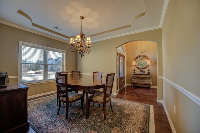 dining area with dark hardwood / wood-style flooring, an inviting chandelier, a raised ceiling, and crown molding