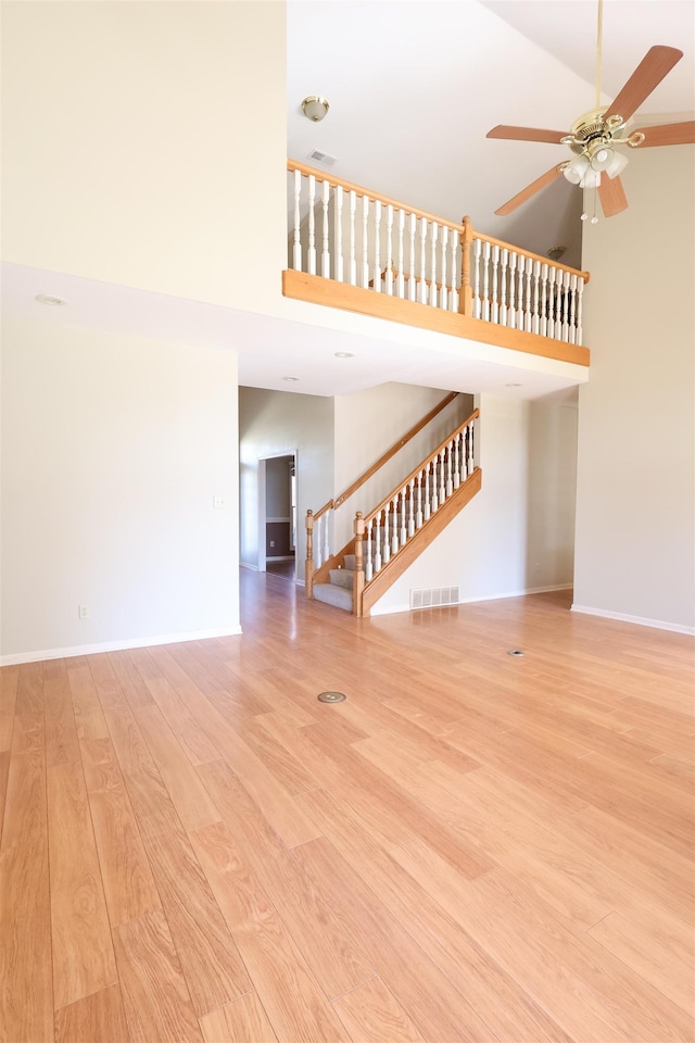 unfurnished living room with ceiling fan, light hardwood / wood-style flooring, and a high ceiling