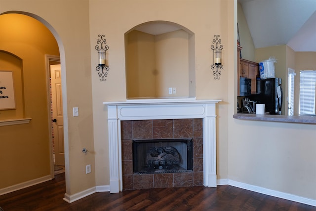 unfurnished living room featuring lofted ceiling, dark wood-type flooring, and a tiled fireplace