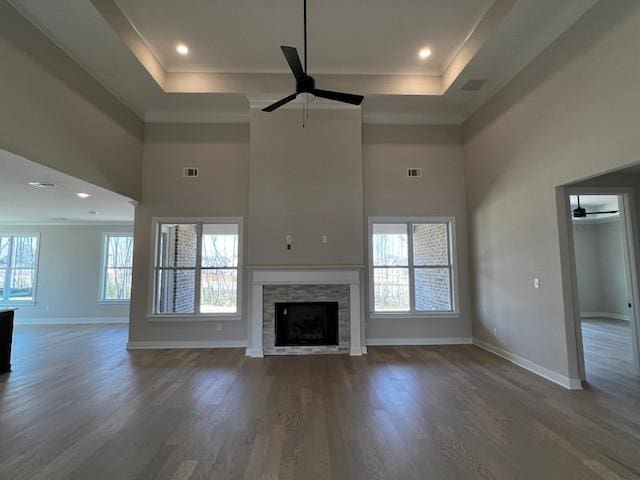 unfurnished living room with ceiling fan, dark hardwood / wood-style flooring, a tiled fireplace, and a tray ceiling