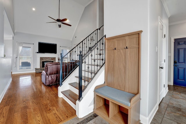 stairway featuring high vaulted ceiling, crown molding, hardwood / wood-style flooring, ceiling fan, and a fireplace