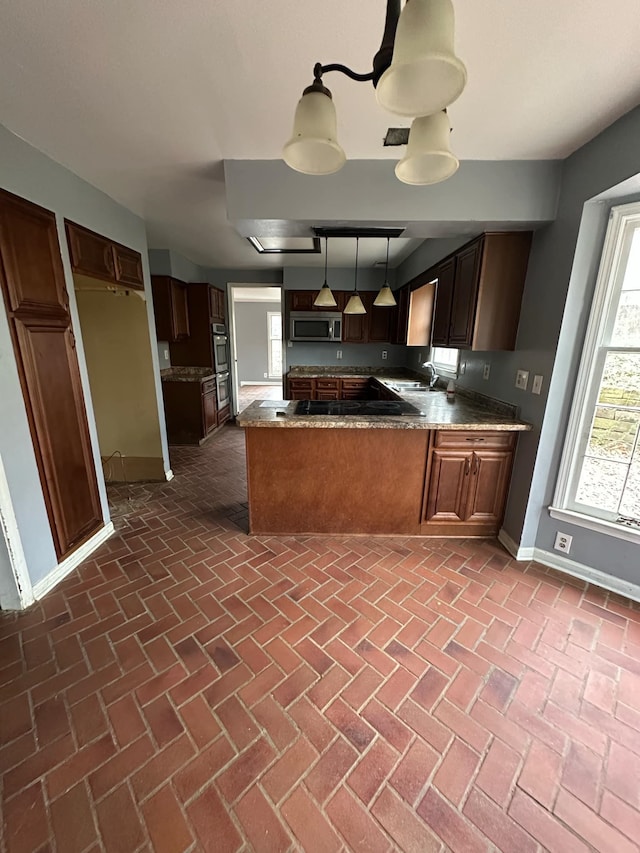 kitchen featuring sink, hanging light fixtures, kitchen peninsula, dark stone counters, and appliances with stainless steel finishes