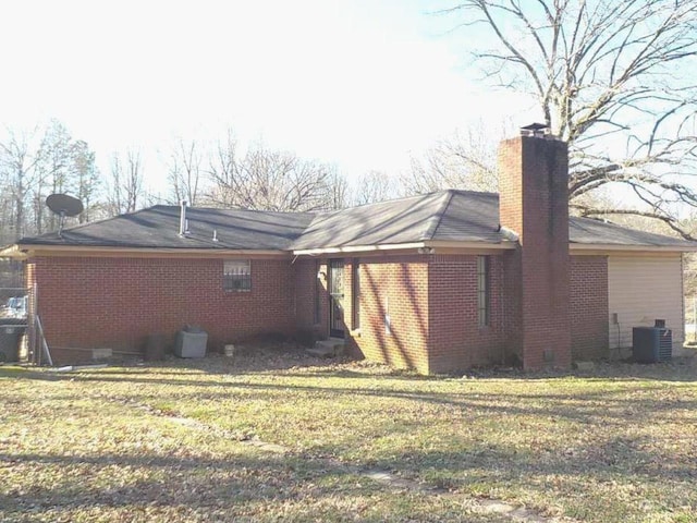 rear view of property with a chimney, brick siding, a lawn, and central AC unit