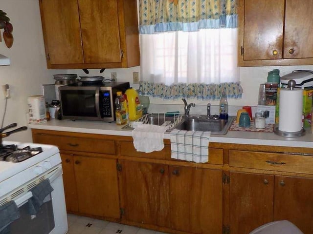 kitchen with brown cabinets, white gas stove, light countertops, stainless steel microwave, and a sink