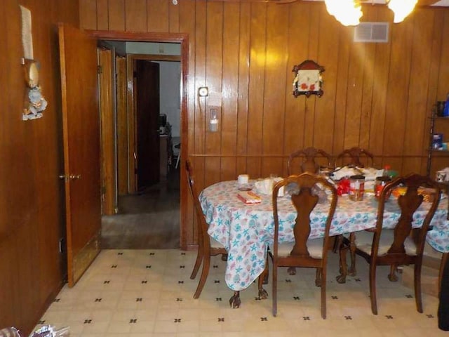 dining space with wood walls, visible vents, light floors, and an inviting chandelier