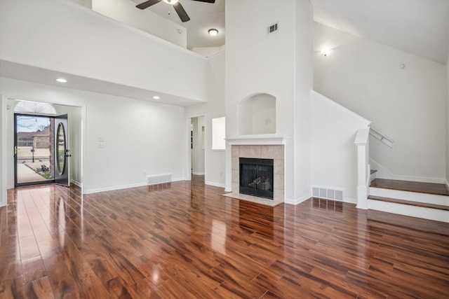 unfurnished living room with ceiling fan, dark hardwood / wood-style floors, a towering ceiling, and a fireplace