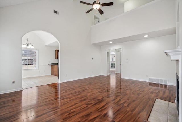 unfurnished living room featuring a tile fireplace, light hardwood / wood-style flooring, high vaulted ceiling, and ceiling fan with notable chandelier