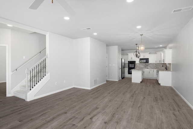 unfurnished living room featuring hardwood / wood-style flooring, ceiling fan with notable chandelier, and sink