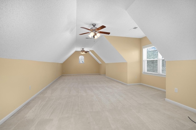 bonus room with light carpet, a textured ceiling, vaulted ceiling, and ceiling fan