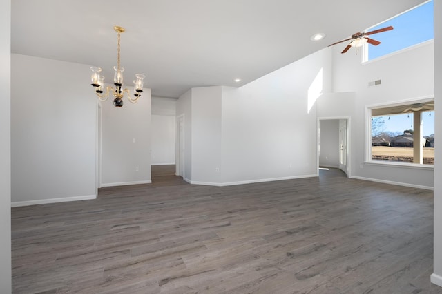 unfurnished living room with hardwood / wood-style floors, a towering ceiling, and ceiling fan with notable chandelier