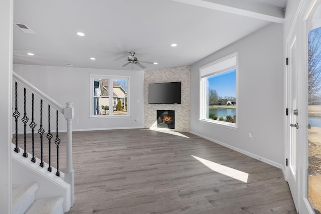 unfurnished living room with beamed ceiling, ceiling fan, light hardwood / wood-style floors, and a fireplace