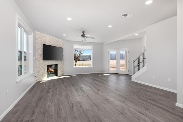 unfurnished living room with ceiling fan, dark hardwood / wood-style flooring, a stone fireplace, and french doors