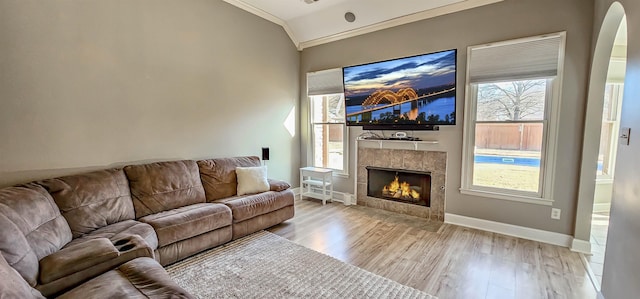 living room featuring a healthy amount of sunlight, ornamental molding, lofted ceiling, a tiled fireplace, and light wood-type flooring