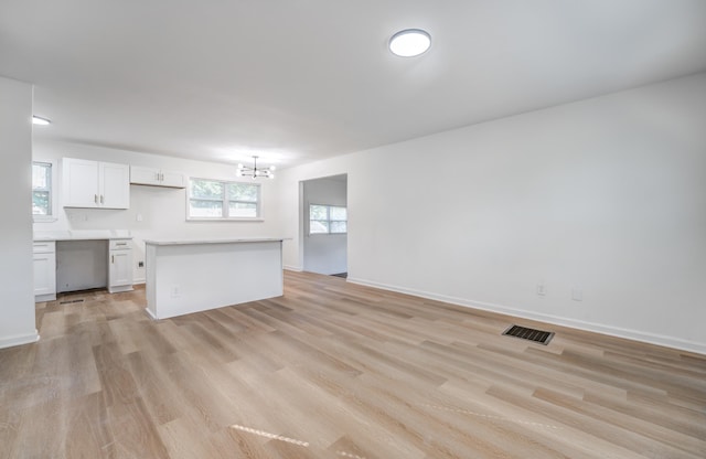 interior space featuring pendant lighting, white cabinets, light hardwood / wood-style floors, a notable chandelier, and a kitchen island