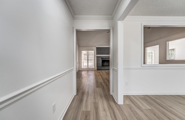 hall with light hardwood / wood-style floors, ornamental molding, and a textured ceiling