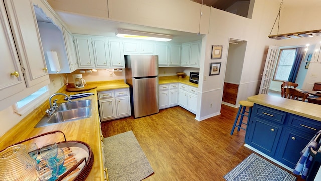 kitchen featuring pendant lighting, sink, light wood-type flooring, white cabinetry, and stainless steel refrigerator