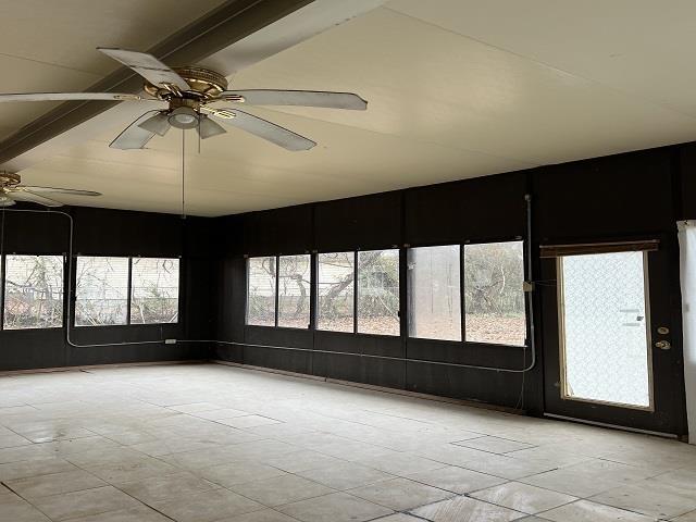 unfurnished sunroom featuring beamed ceiling and ceiling fan