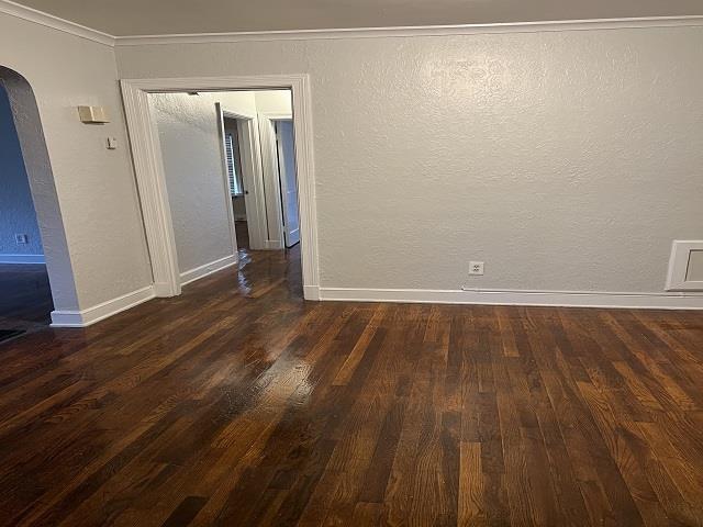 empty room with dark hardwood / wood-style flooring and crown molding