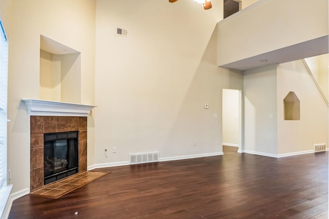 unfurnished living room featuring ceiling fan, dark hardwood / wood-style floors, a towering ceiling, and a tiled fireplace