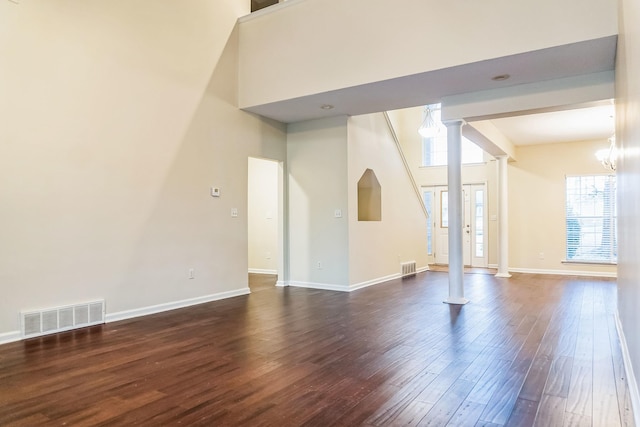 spare room featuring dark hardwood / wood-style floors, an inviting chandelier, and ornate columns