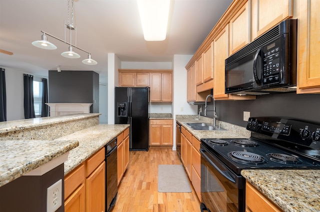 kitchen with sink, pendant lighting, light stone counters, and black appliances